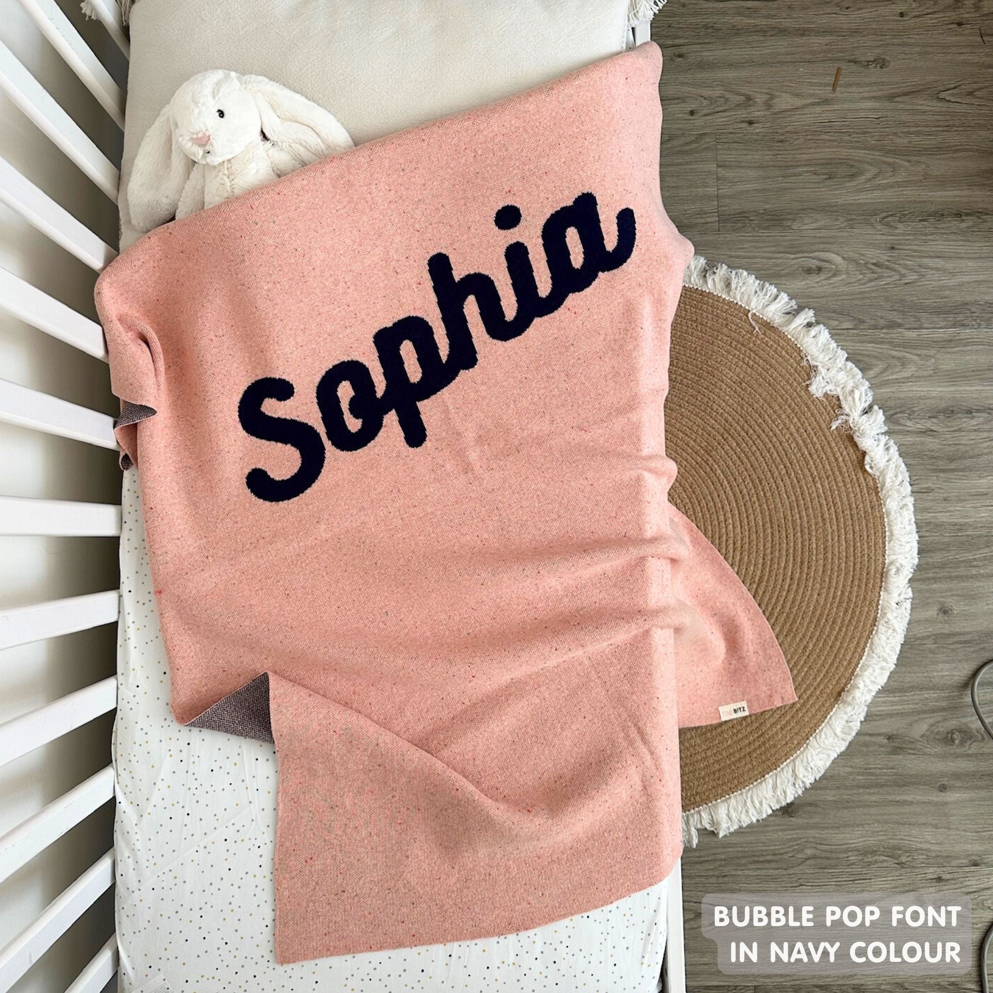 Knitted baby blanket in pink and navy with a confetti pattern, customised with baby's name, made by TinyBitz.