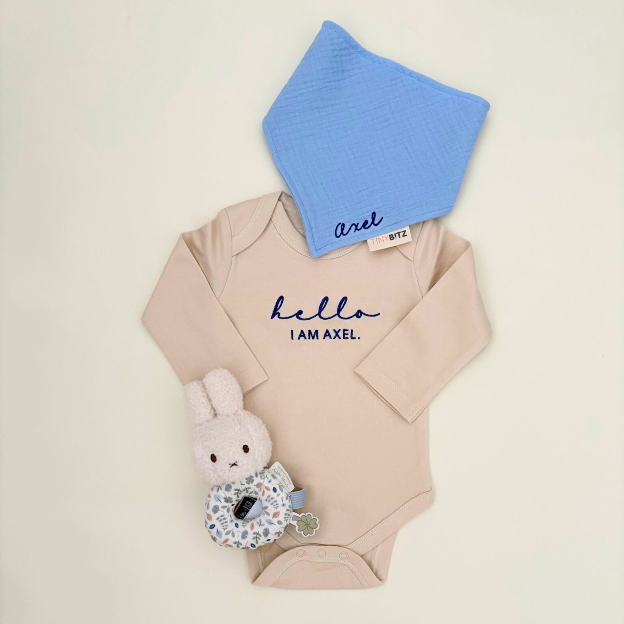 Personalised baby gift set with embroidered onesie, muslin bib, and floral Miffy rattle toy, all neatly packed in a pastel gift box for newborn gifting.