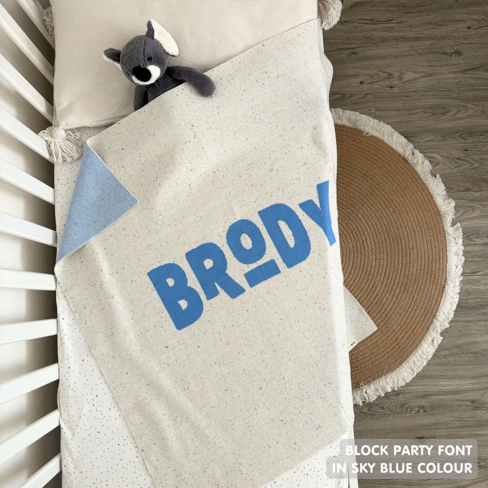 Cotton baby blanket with baby's name knitted in cream and sky blue with a confetti pattern, made by TinyBitz.