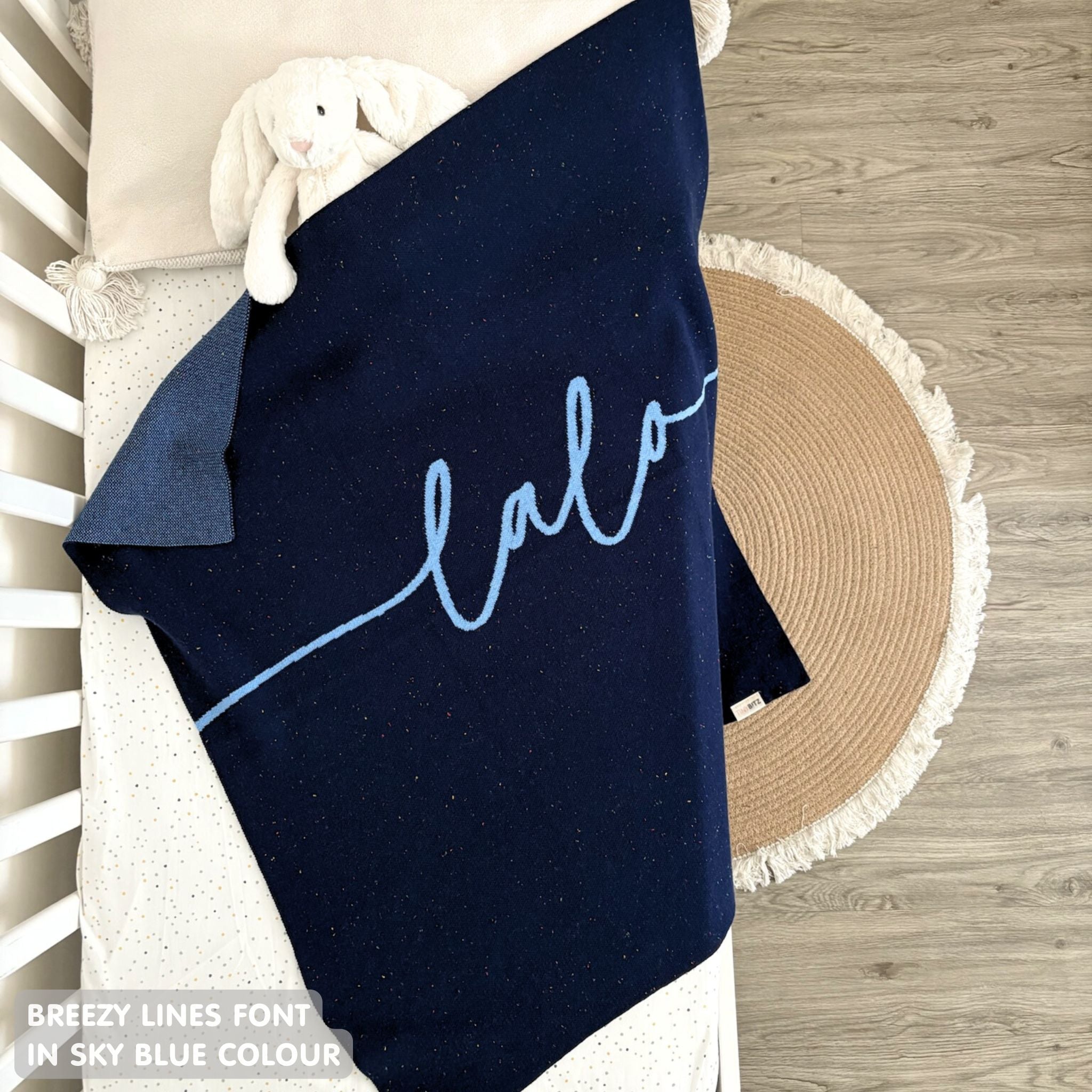 Cotton baby blanket with baby's name knitted in navy and sky blue with a confetti pattern, made by TinyBitz.