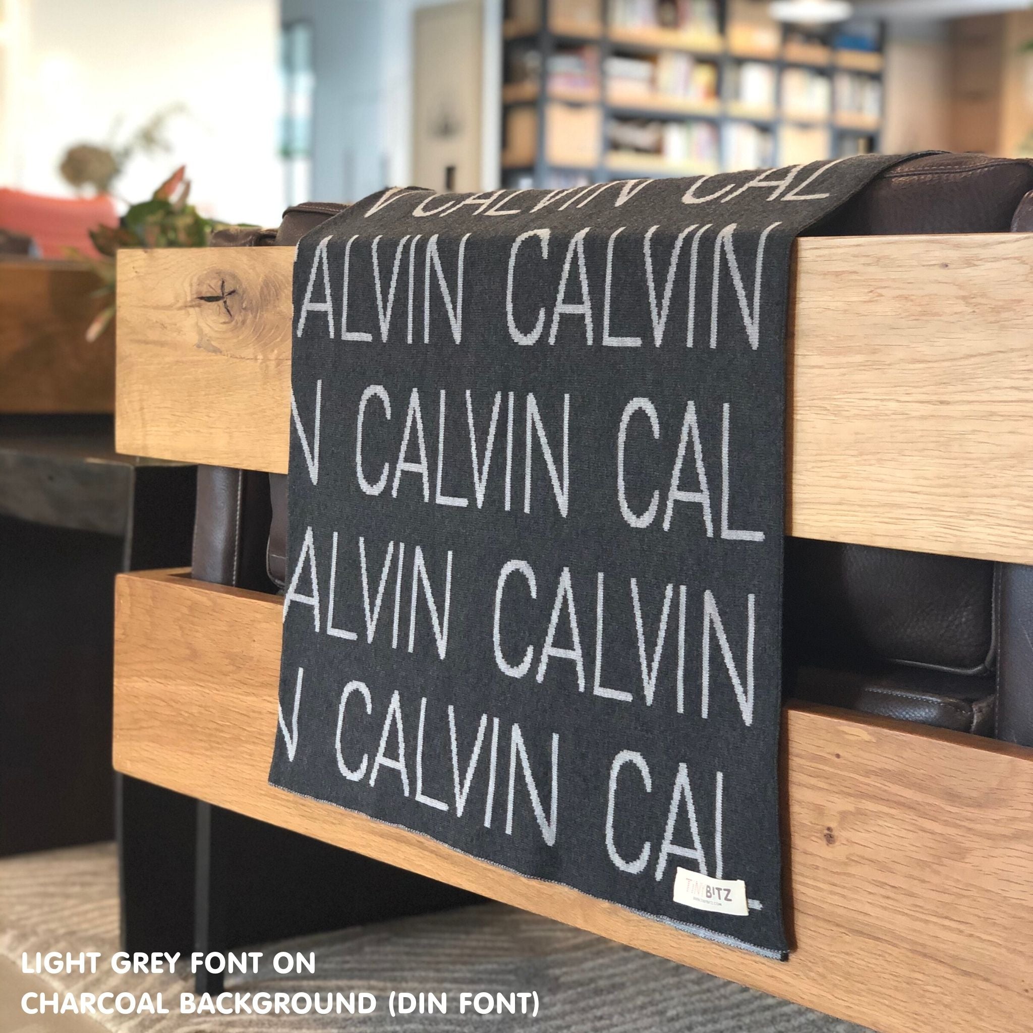 Custom name blanket in charcoal and light grey draped over a chair makes the best personalized home decor.