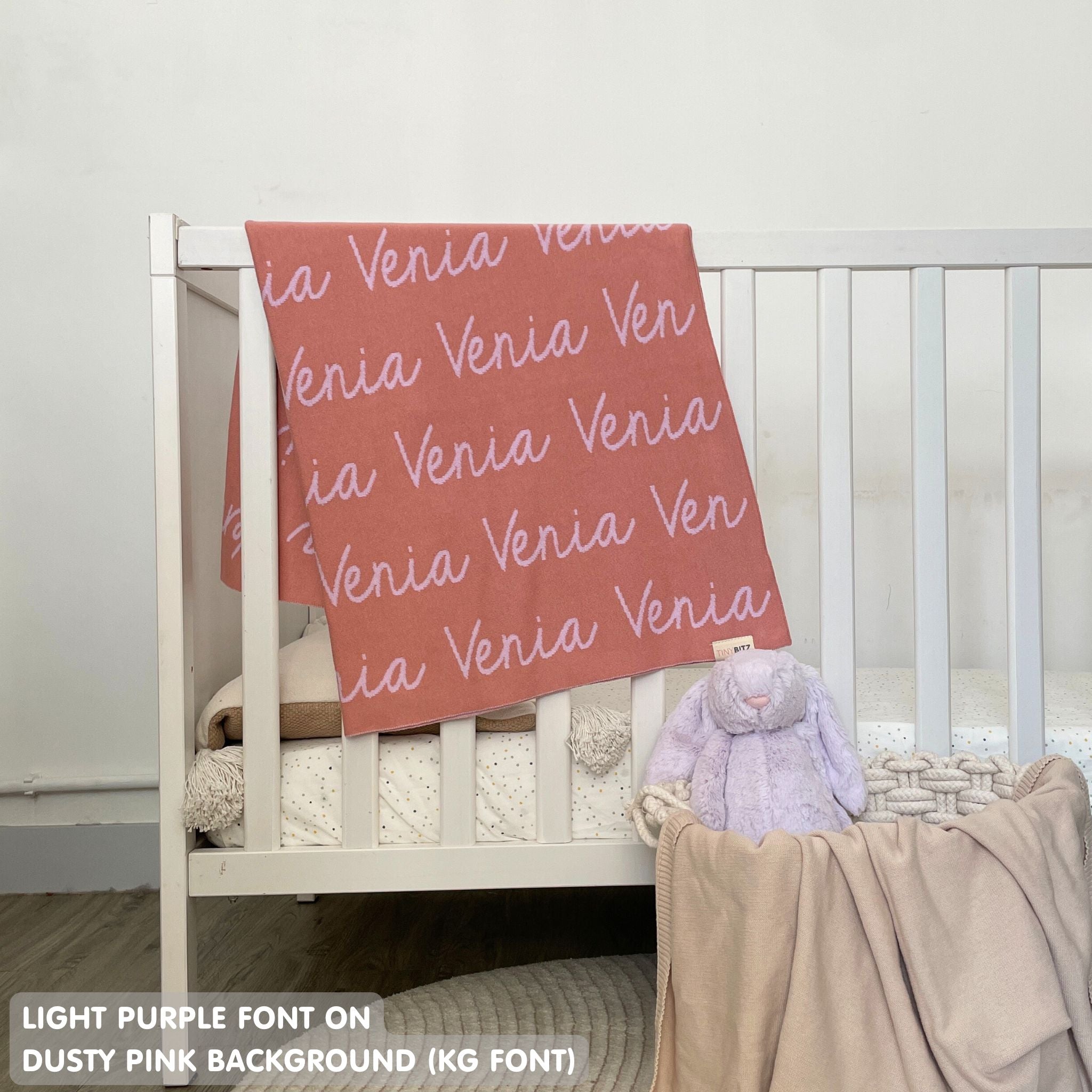 TinyBitz knitted baby girls blanket in dusty pink background and light purple, personalized with your baby’s name.