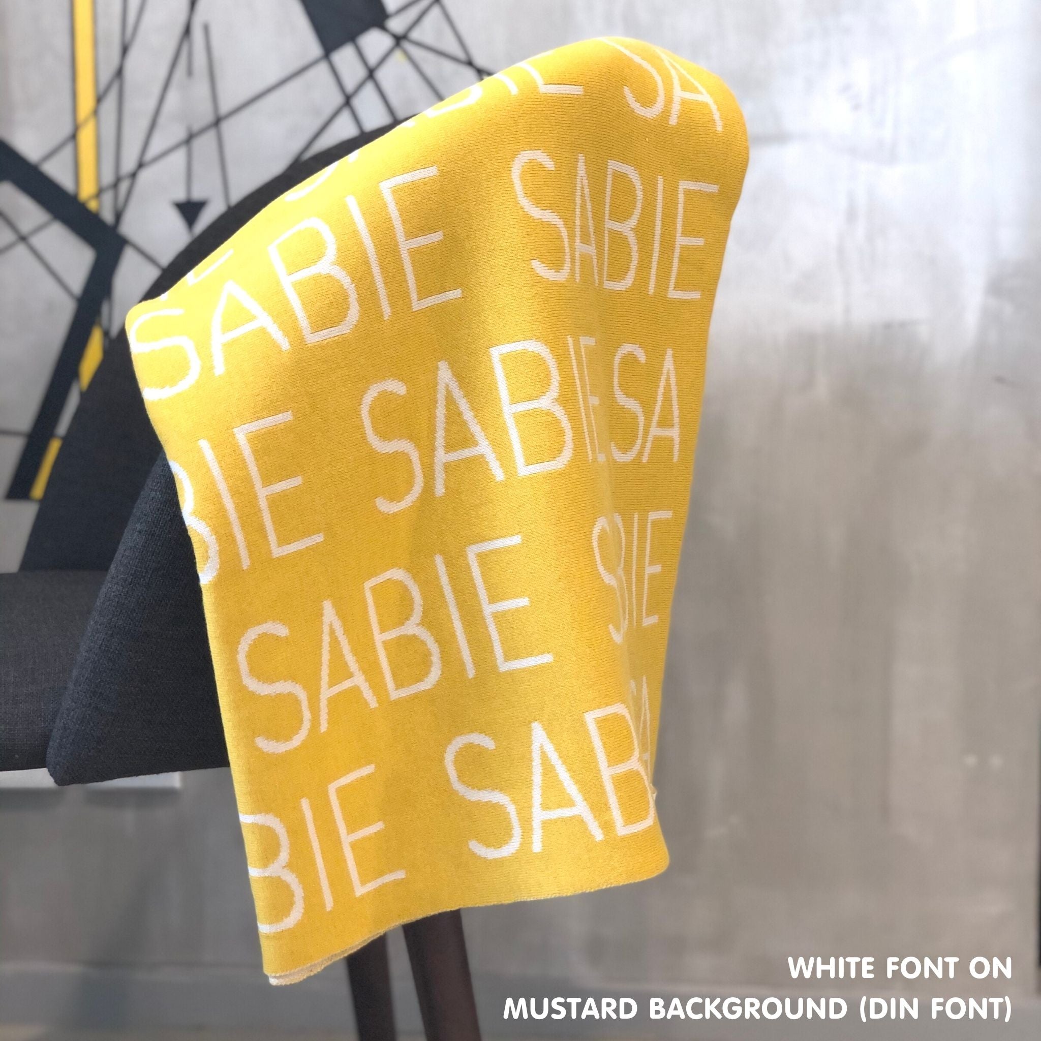 Custom name blanket in mustard and white draped over a chair makes the best personalized home decor.