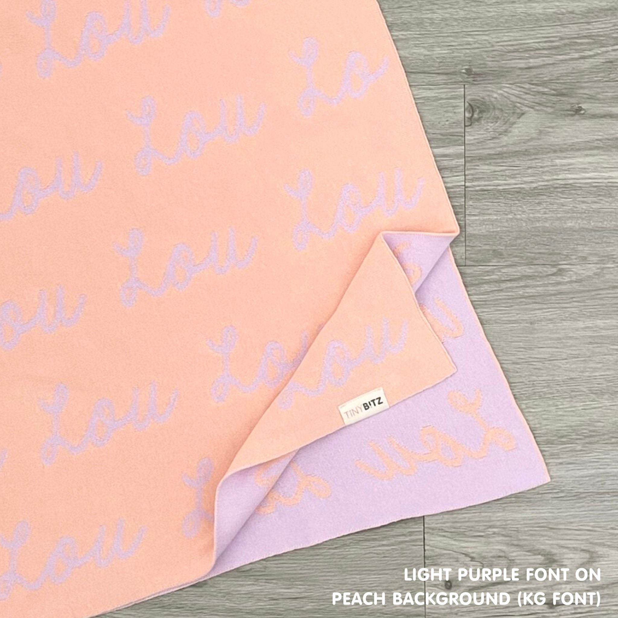 Cotton baby blanket with baby's name knitted in peach and light purple, made by TinyBitz.