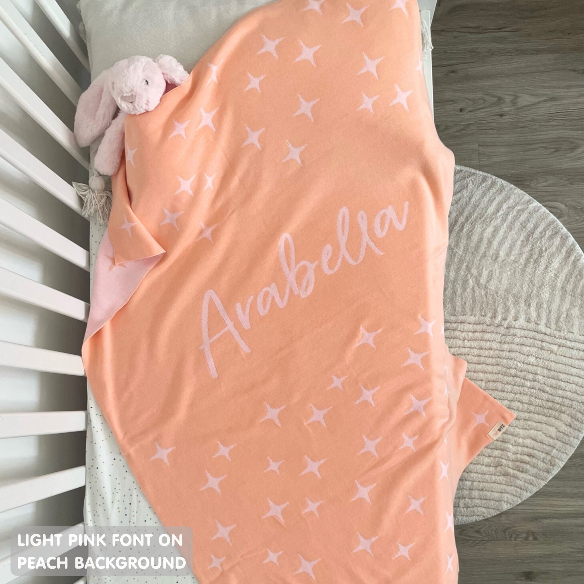 Knitted baby blanket in peach and light pink with a twinkles pattern, customised with baby's name, made by TinyBitz.