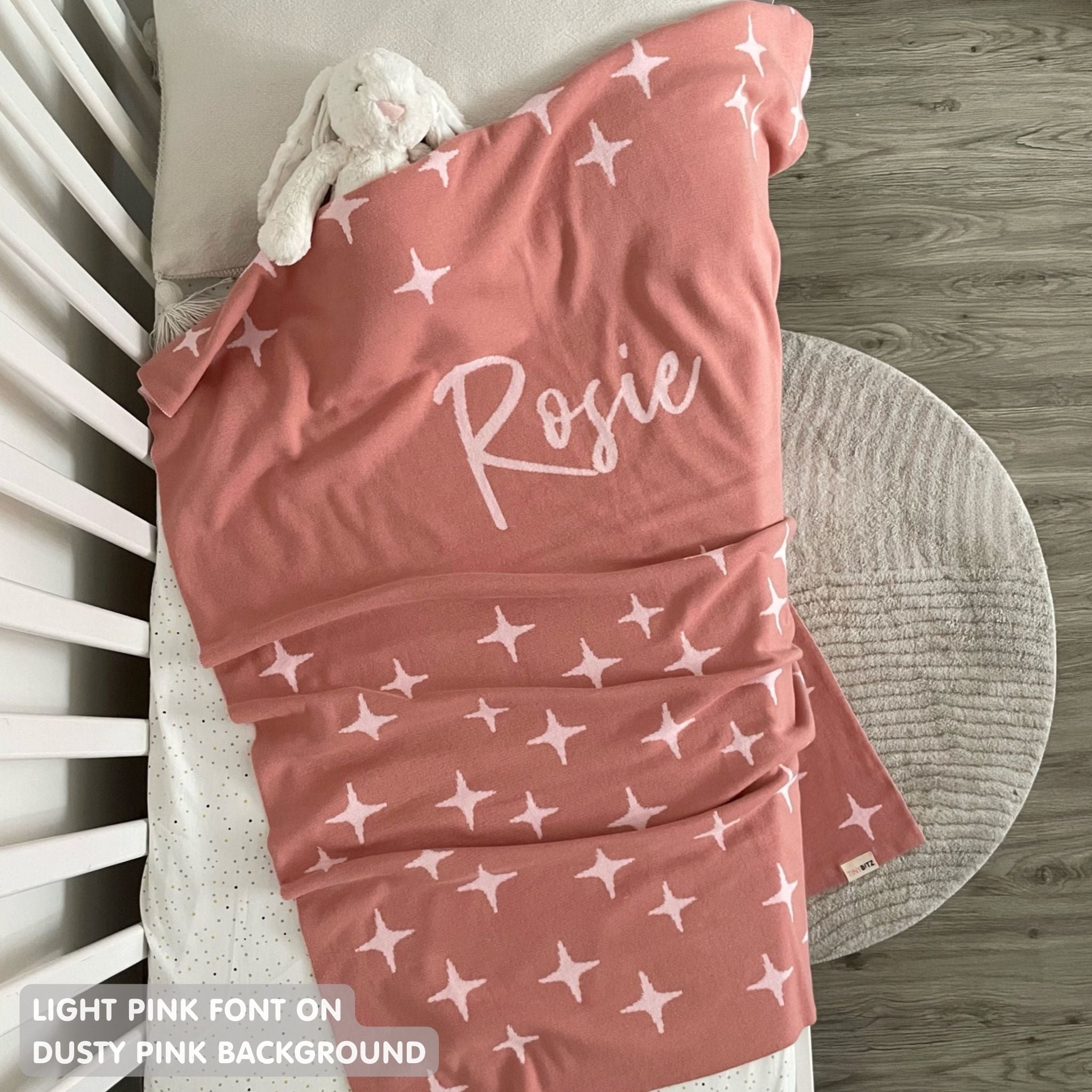 Knitted baby blanket in dusty pink and light pink with a twinkles pattern, customised with baby's name, made by TinyBitz.