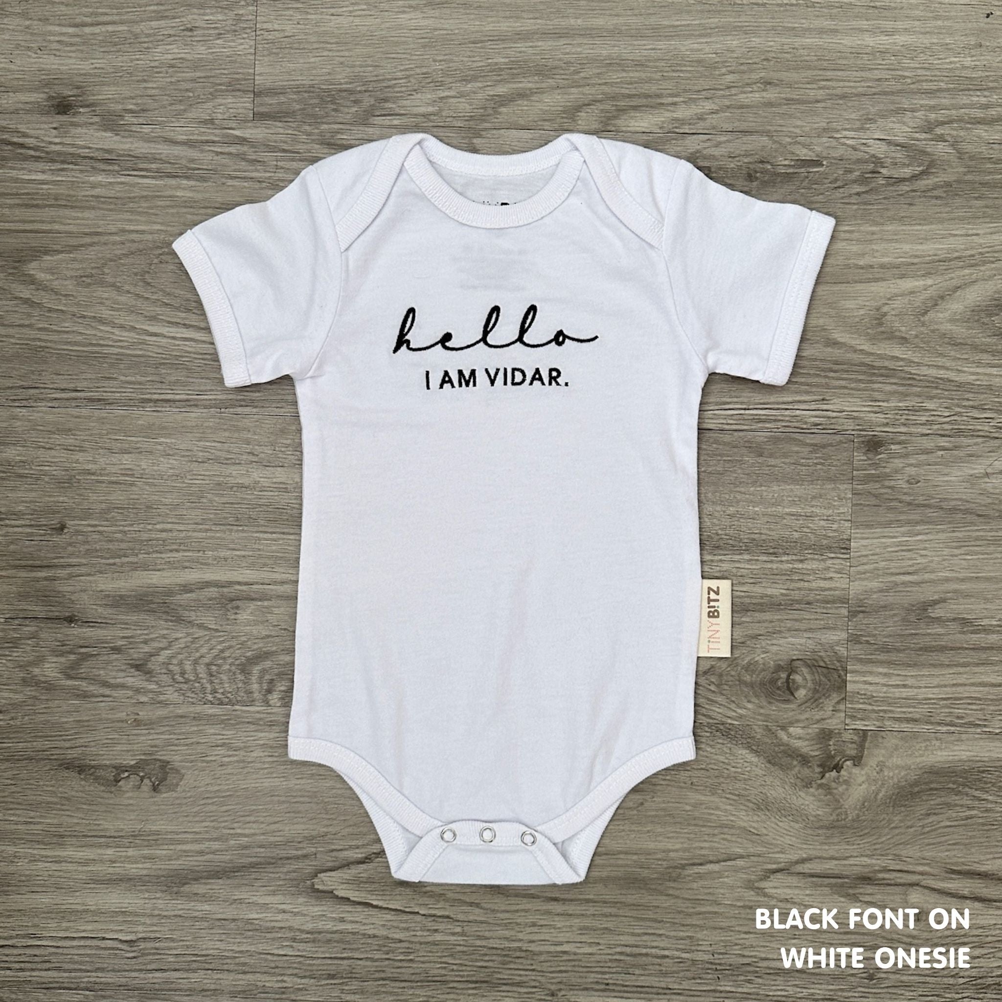 Neutral-tone personalised baby onesie featuring custom name, made-to-order newborn gift by TinyBitz.