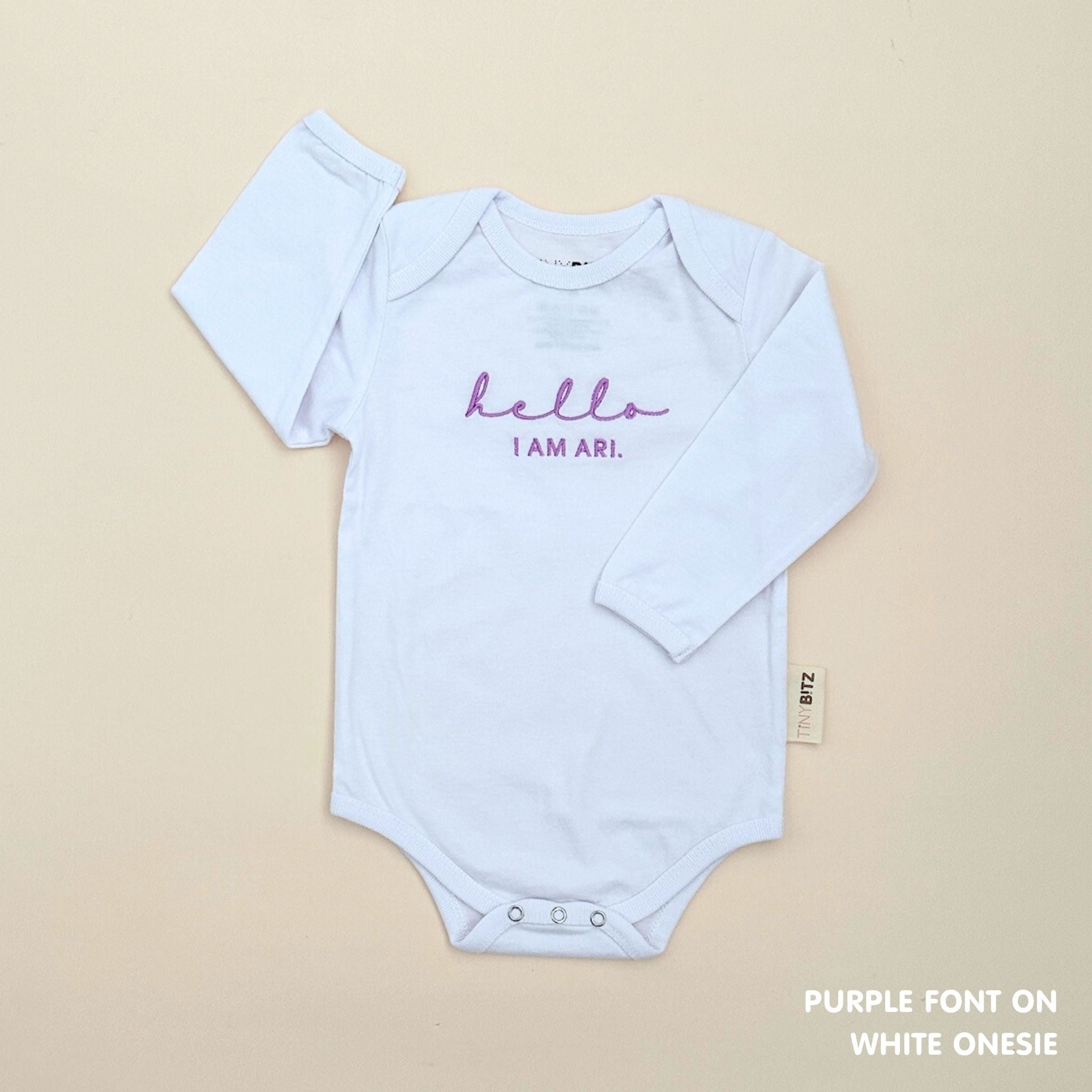 Minimalist personalised onesie in neutral tones with name embroidery, styled for newborn birth announcements by TinyBitz.