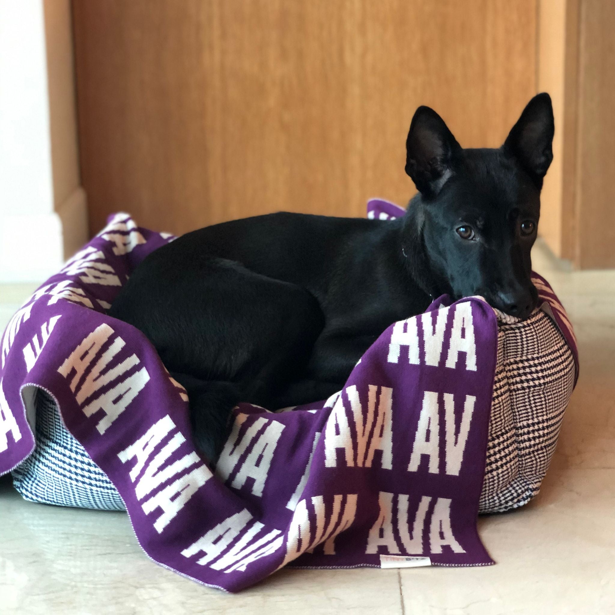 Personalised pet blanket in eggplant and white knitted cotton, custom dog blanket by TinyBitz, styled on modern wooden dog bed.