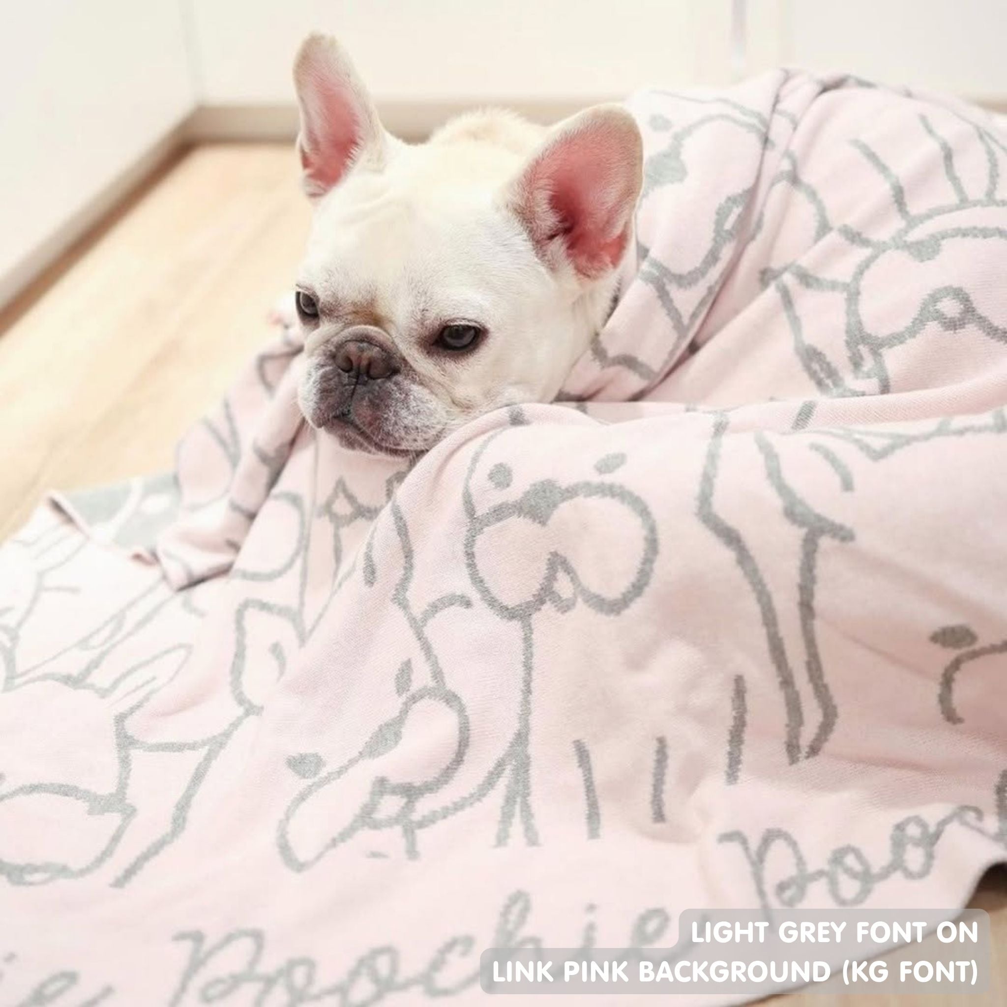 Personalised pet blanket for Frenchie in light pink and light grey knitted cotton, custom dog blanket by TinyBitz, styled on modern wooden dog bed.