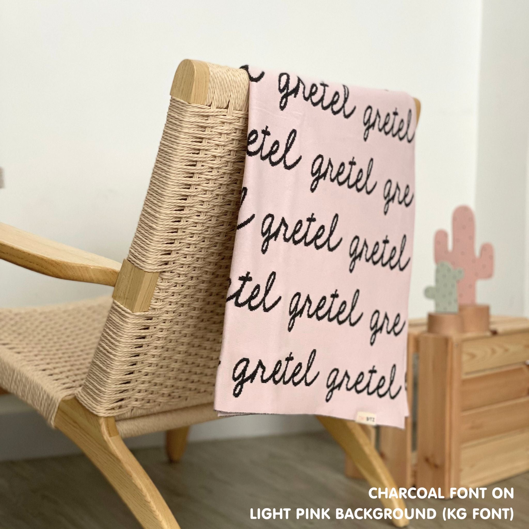 Personalised pet blanket in light pink and charcoal knitted cotton, custom dog blanket by TinyBitz, styled on modern wooden dog bed.