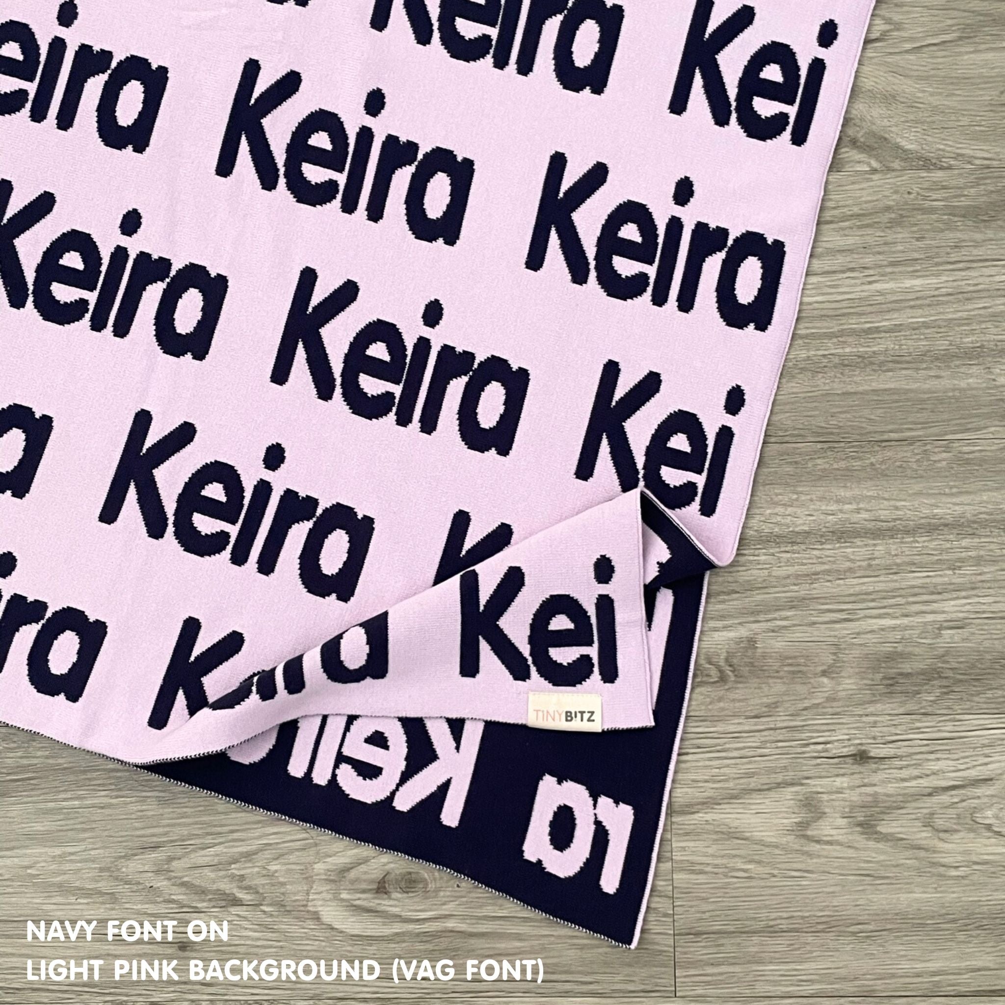 Personalised pet blanket in light pink and navy knitted cotton, custom dog blanket by TinyBitz, styled on modern wooden dog bed.