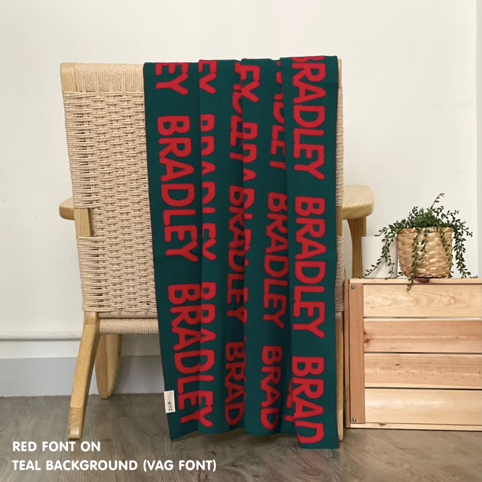 Personalised pet blanket in teal and red knitted cotton, custom dog blanket by TinyBitz, styled on modern wooden dog bed.