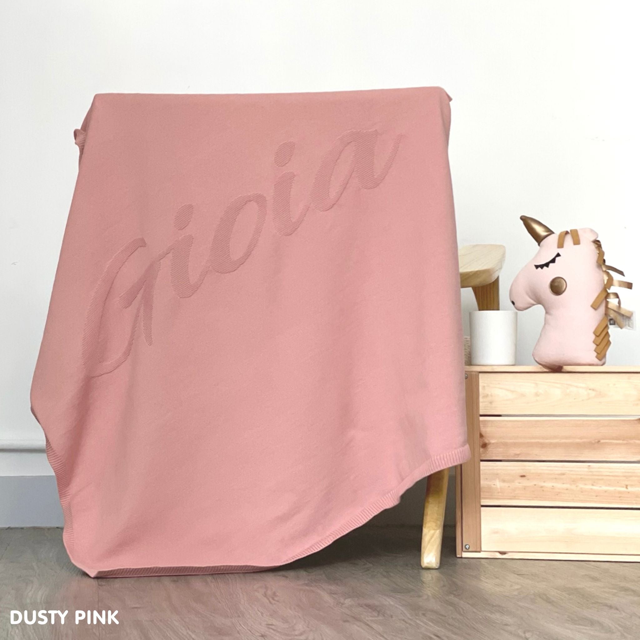 TinyBitz personalized knitted blanket in dusty pink background, customized with baby's name and made from 100% cotton.
