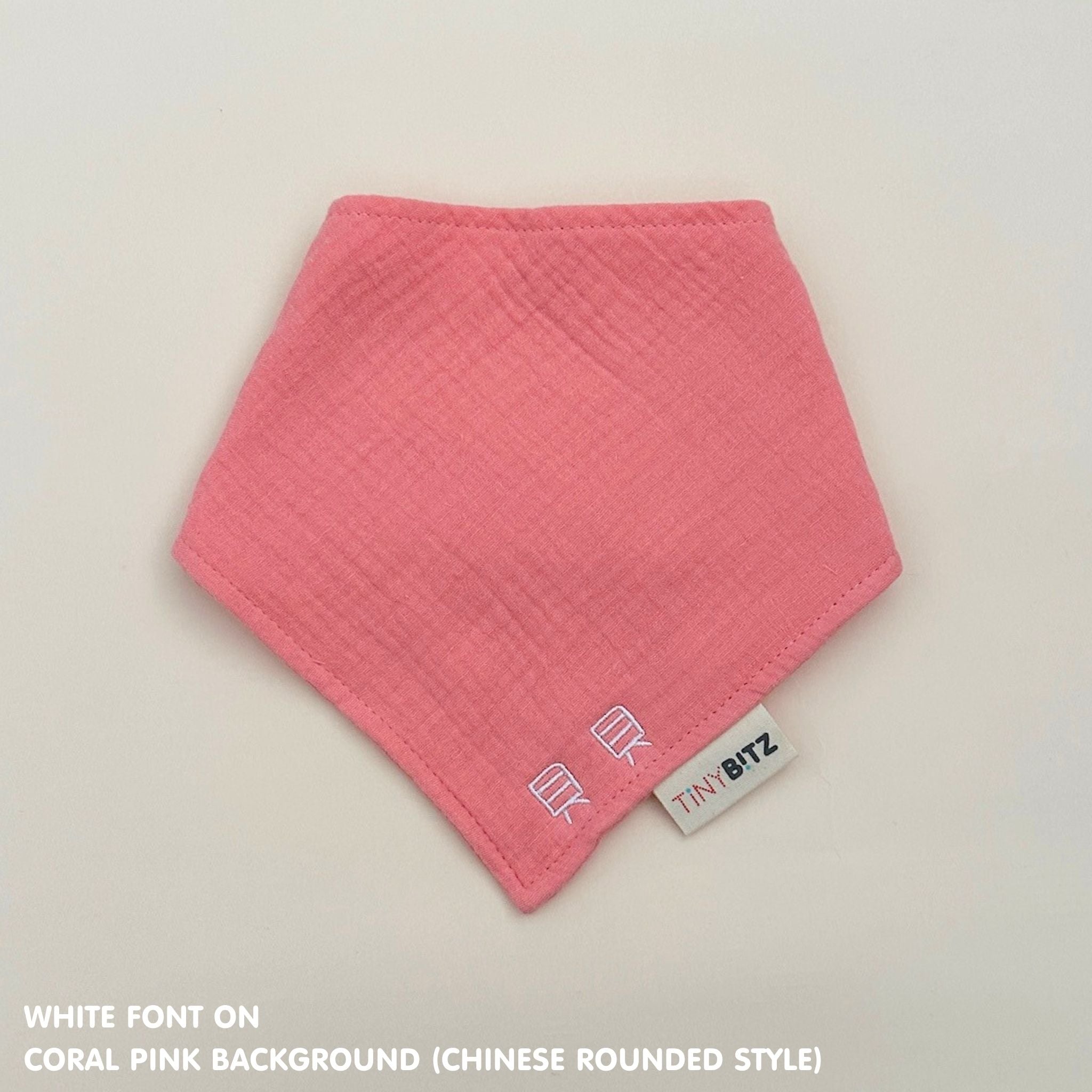 Personalized coral pink organic muslin bib with custom name embroidery, perfect for baby gifts and keepsake accessories.
