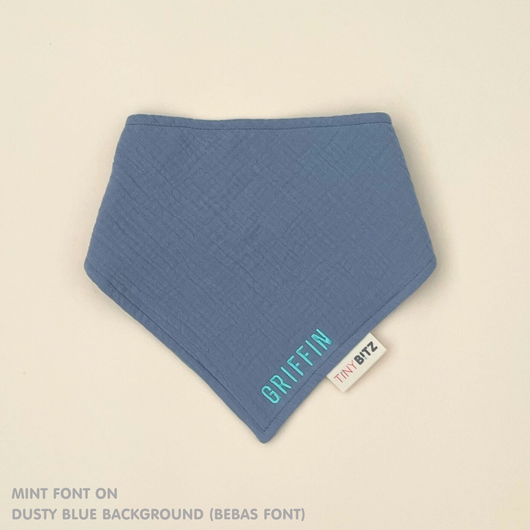 Personalized dusty blue organic muslin bib with custom name embroidery, perfect for baby gifts and keepsake accessories.