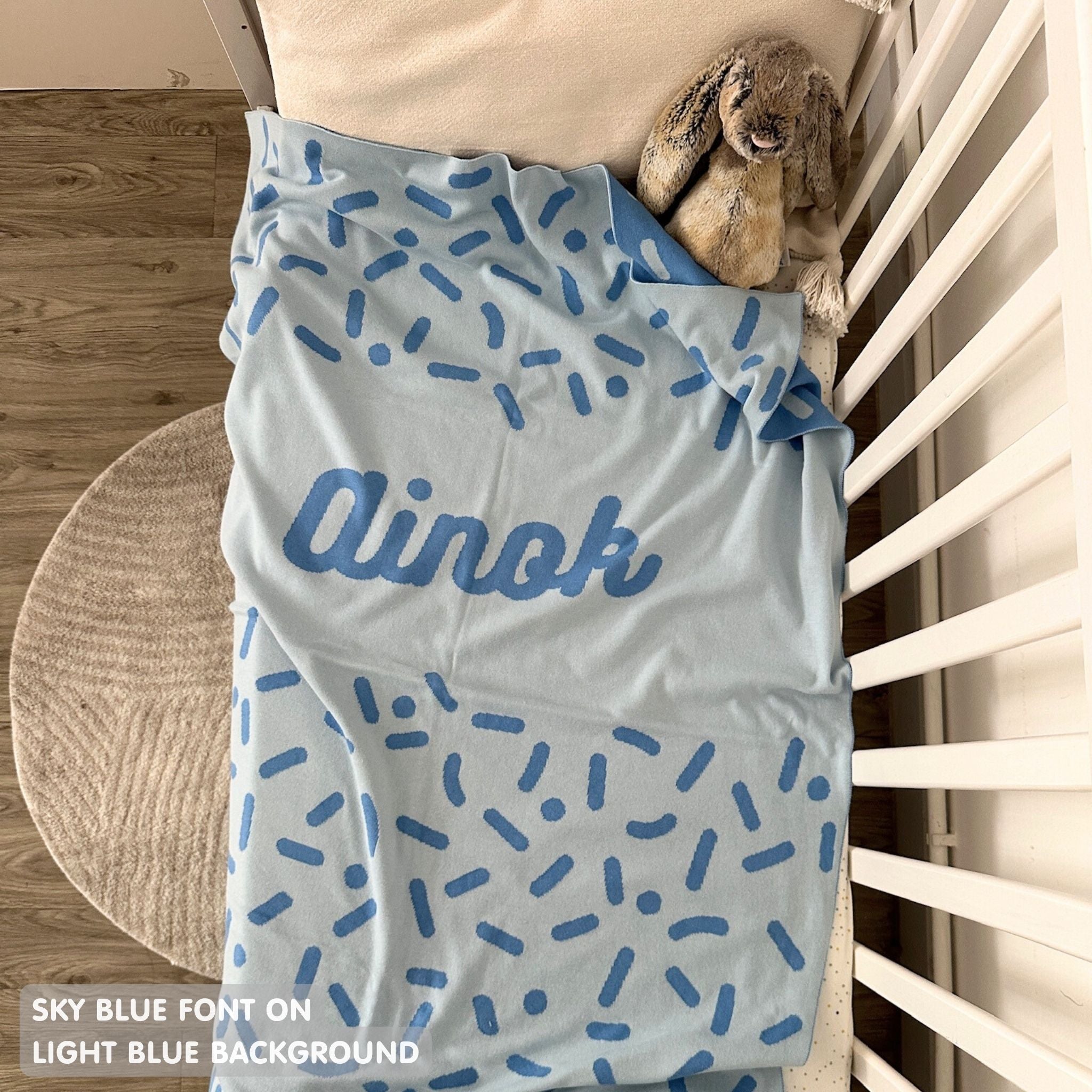 Knitted baby blanket in light blue and sky blue with a confetti pattern, customised with baby's name, made by TinyBitz.