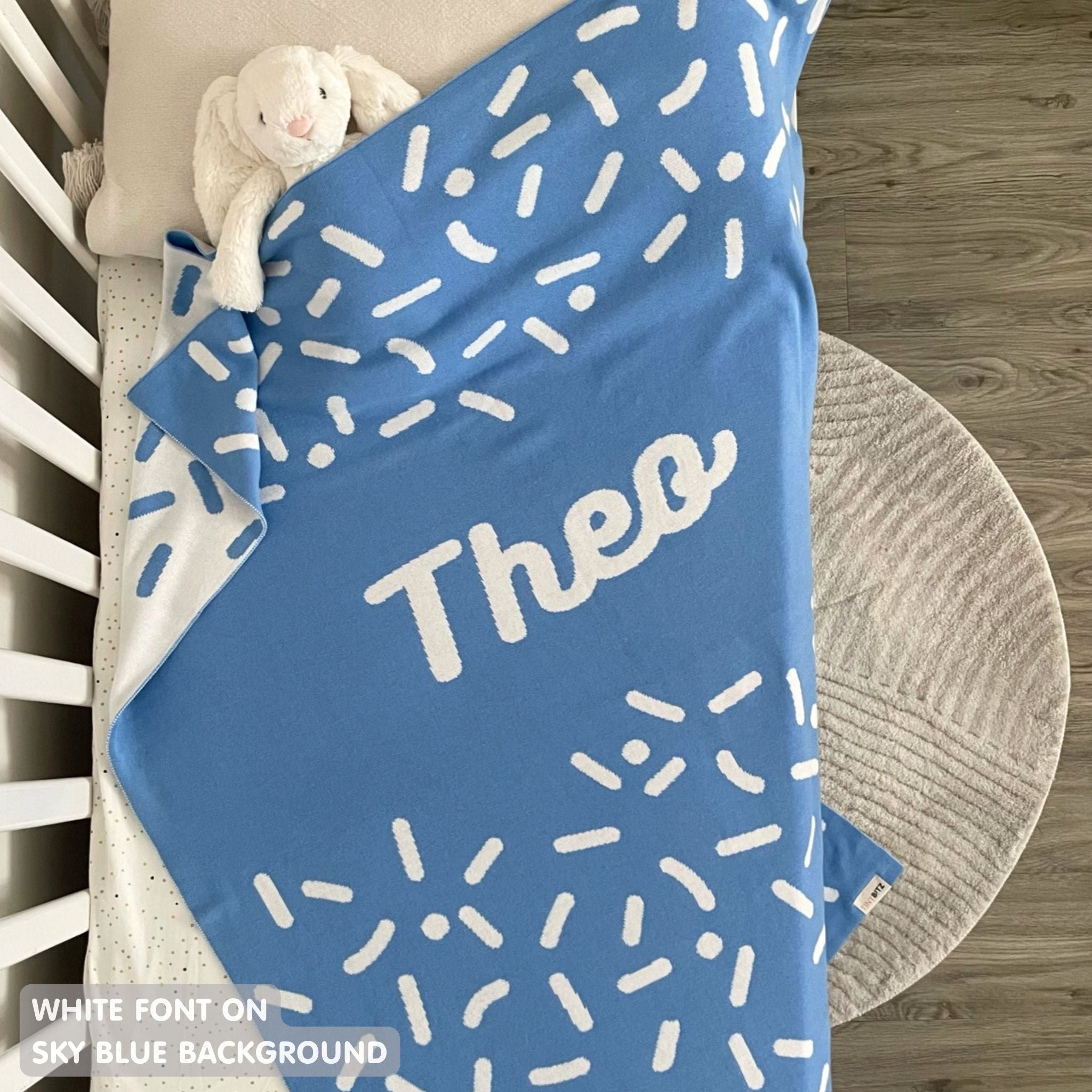 Knitted baby blanket in sky blue and white with a confetti pattern, customised with baby's name, made by TinyBitz.