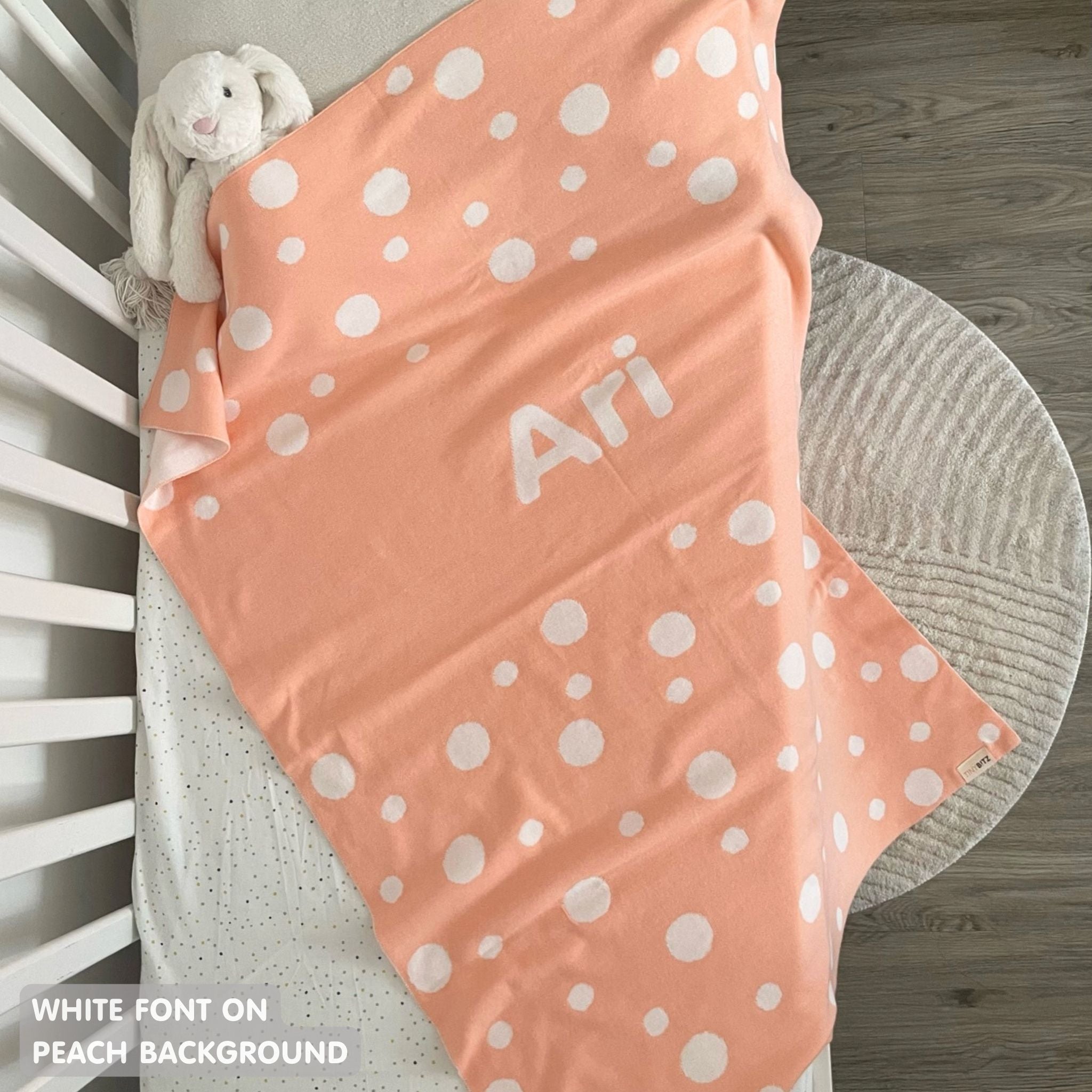 Knitted baby blanket in peach and white with a dot pattern, customised with baby's name, made by TinyBitz.