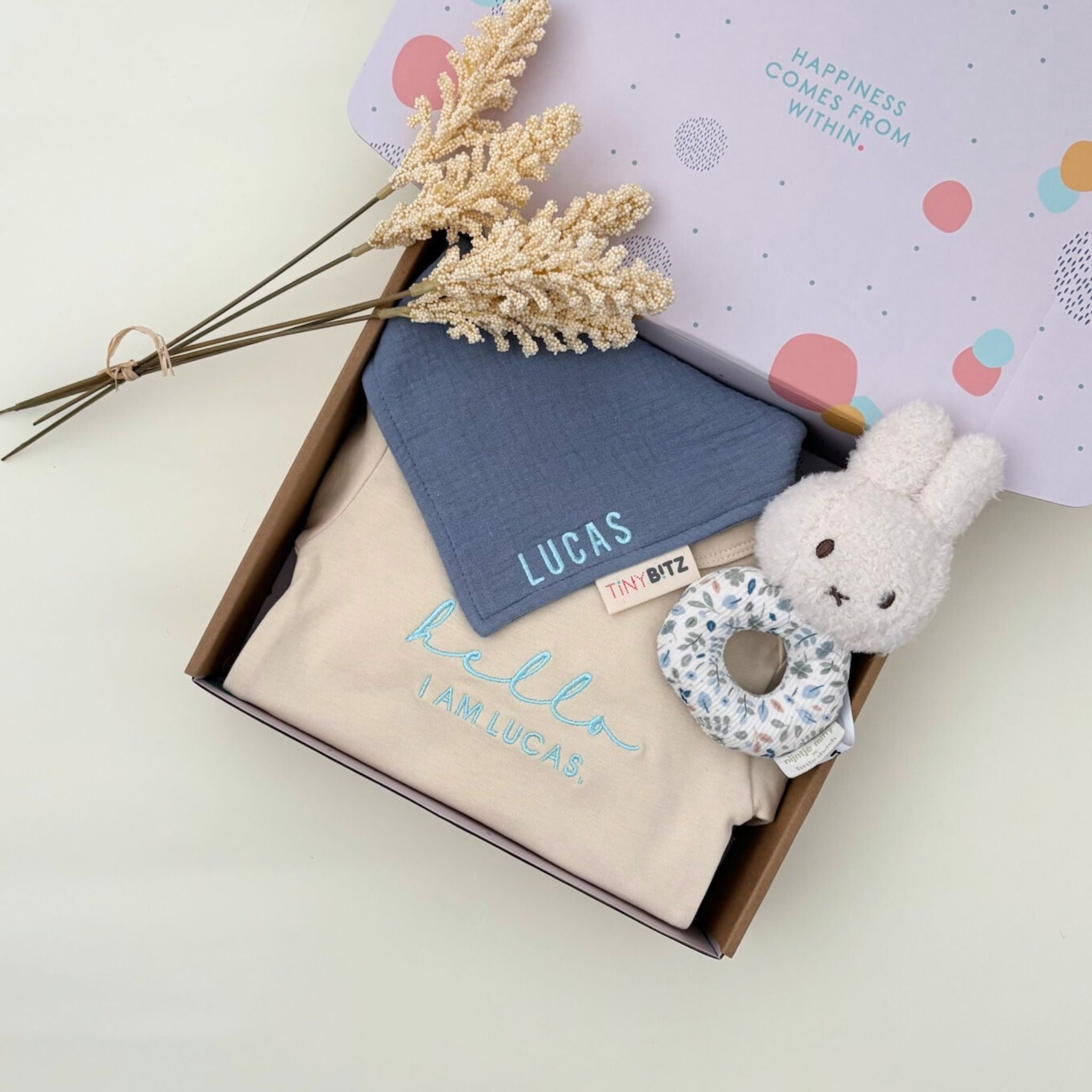 Personalised baby gift set with embroidered onesie, muslin bib, and floral Miffy rattle toy, all neatly packed in a pastel gift box for newborn gifting.