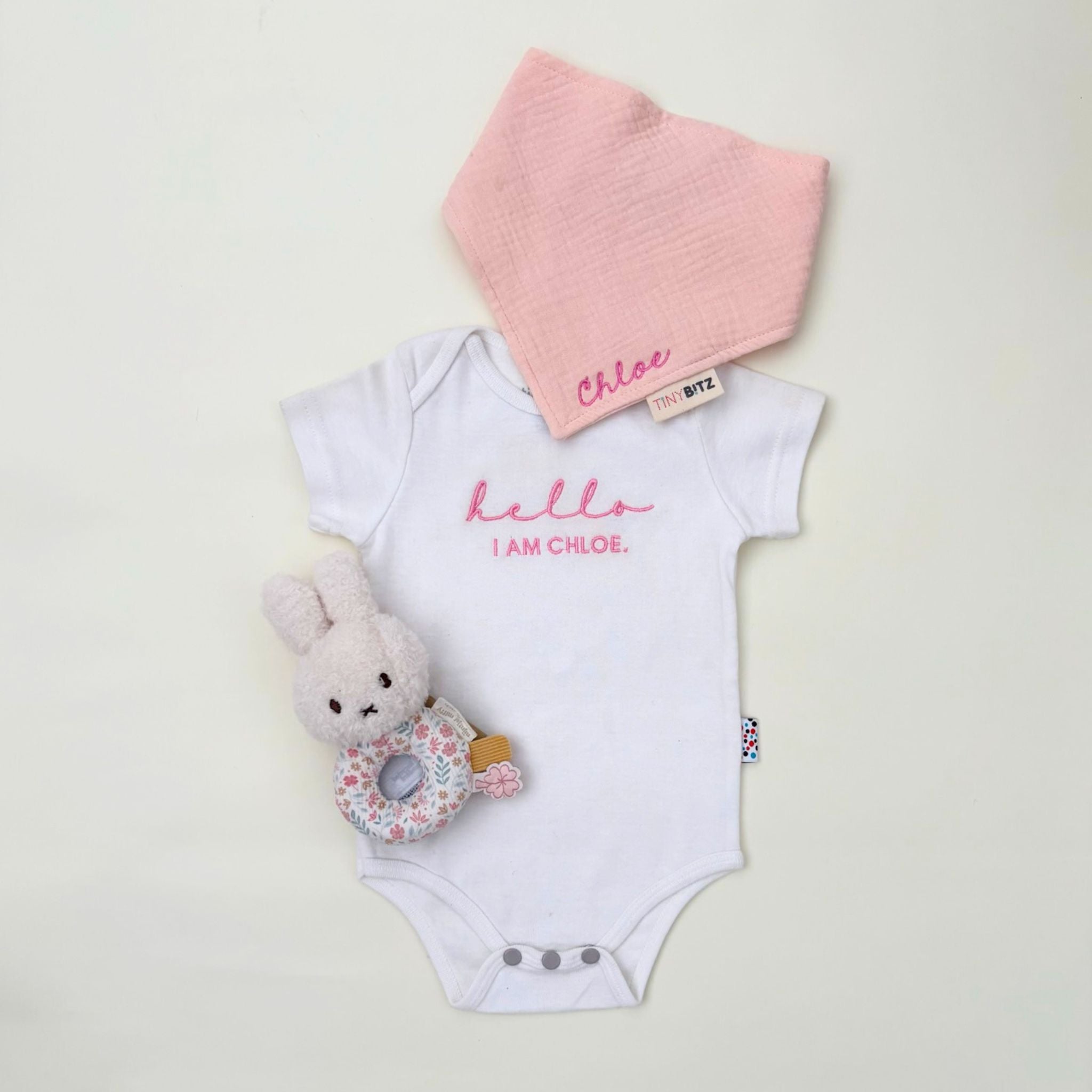 Personalised baby gift set with embroidered onesie, muslin bib, and floral Miffy rattle toy, all neatly packed in a pastel gift box for newborn gifting.