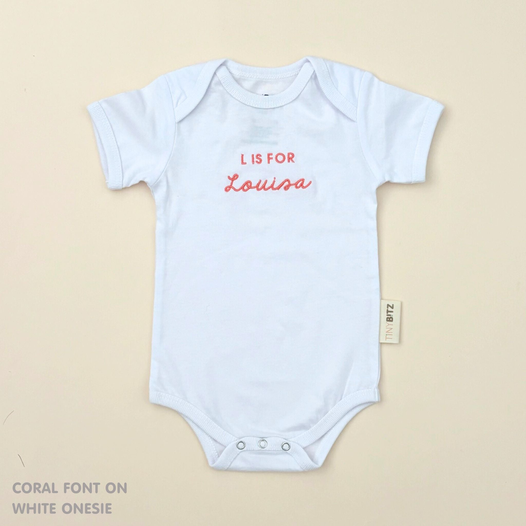 Minimalist personalised onesie in neutral tones with name embroidery, styled for newborn birth announcements by TinyBitz.