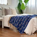 Custom name blanket draped on bed, knitted in blue and oatmeal makes the best personalised home decor.
