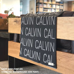 Custom name blanket in charcoal and light grey draped over a chair makes the best personalized home decor.