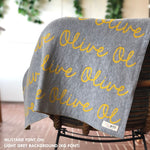 Custom name blanket in light grey and musatrd draped over a chair makes the best personalized home decor.