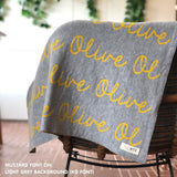 Custom name blanket in light grey and musatrd draped over a chair makes the best personalized home decor.