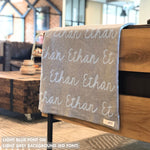 Custom name blanket in light grey and light blue draped over a chair makes the best personalized home decor.