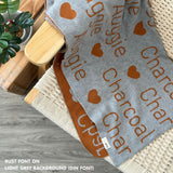 TinyBitz custom name blanket with couple's name knitted in light grey and rust, making the perfect engagement gift!