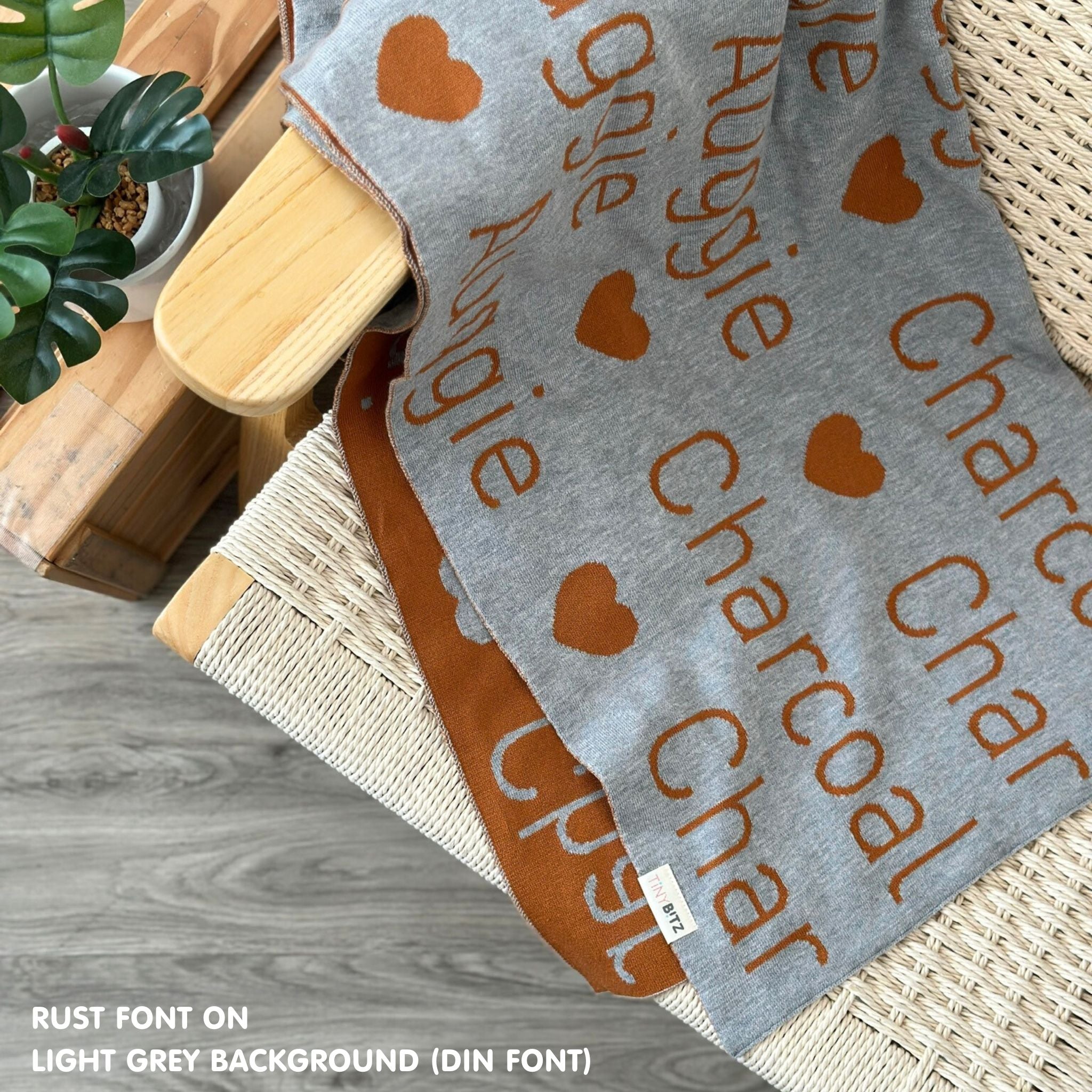 TinyBitz custom name blanket with couple's name knitted in light grey and rust, making the perfect engagement gift!