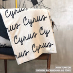 Custom name blanket in oatmeal and navy draped over a chair makes the best personalized home decor.