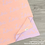 Cotton baby blanket with baby's name knitted in peach and light purple, made by TinyBitz.