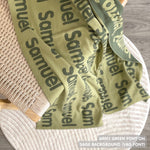 Custom name blanket draped on chair, knitted in sage and army green makes the best personalised home decor.