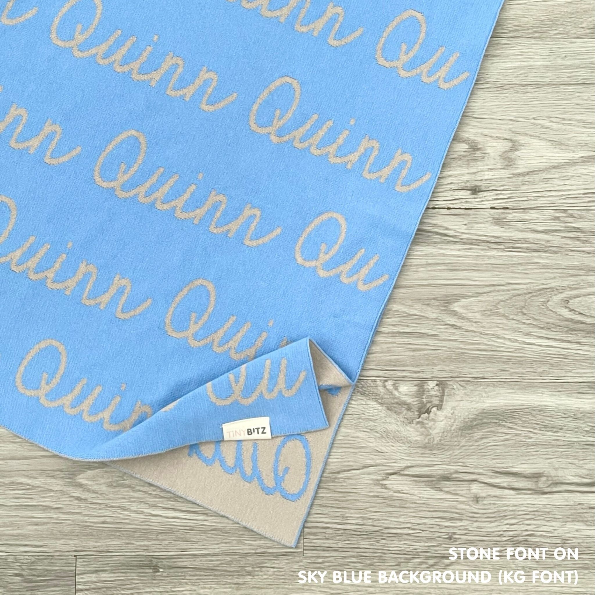 Customisable blanket with adult's name knitted in sky blue and stone, personalized by TinyBitz.
