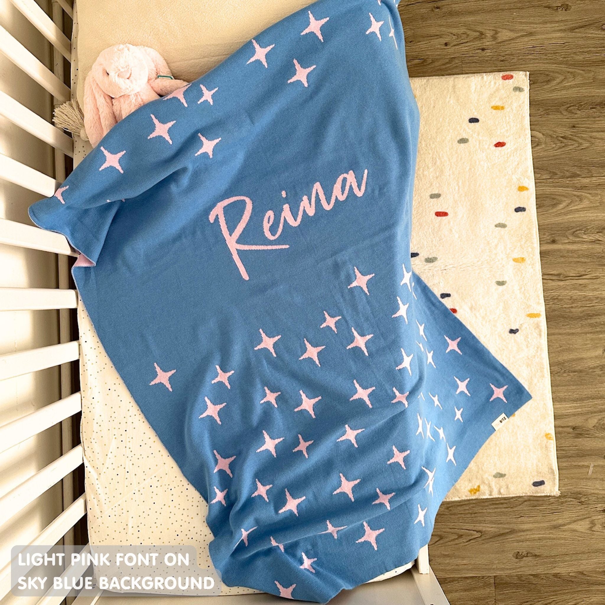 Cotton baby blanket with baby's name knitted in sky blue and light pink with a twinkles pattern, made by TinyBitz.