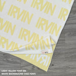 Customisable blanket with adult's name knitted in white and light yellow, personalized by TinyBitz.